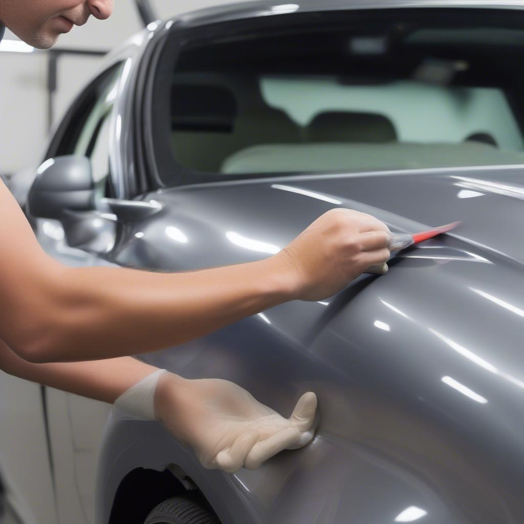 Kỹ thuật sửa vỏ xe ô tô: Minh họa kỹ thuật PDR (Paintless Dent Repair) đang được thực hiện trên một vết lõm nhỏ trên thân xe. Hình ảnh cho thấy kỹ thuật viên đang sử dụng các dụng cụ chuyên dụng để đẩy vết lõm từ bên trong ra ngoài mà không cần sơn lại.